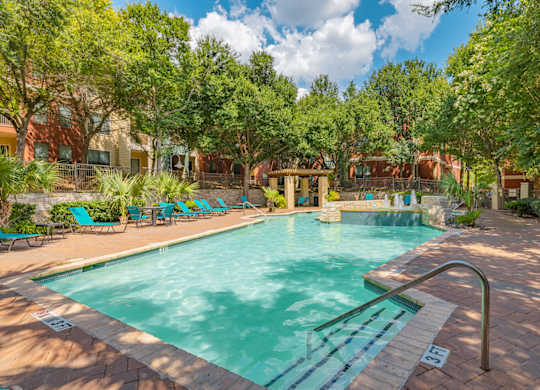 A swimming pool surrounded by trees and lounge chairs.