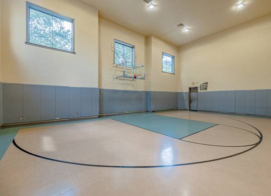 A basketball court inside a gym with a basketball hoop and a bench.