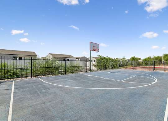 A basketball court with a red hoop and a black fence.