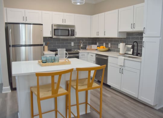 a kitchen with white cabinets and a counter with two chairs