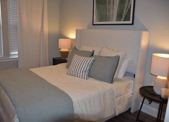 A bed with a grey blanket and pillows is in a room with two lamps on side tables.