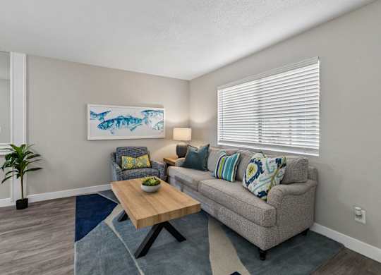 A living room with a grey couch, a wooden coffee table, and a painting of a fish on the wall.
