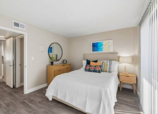 A bedroom with a bed, nightstand, and a mirror on the wall.