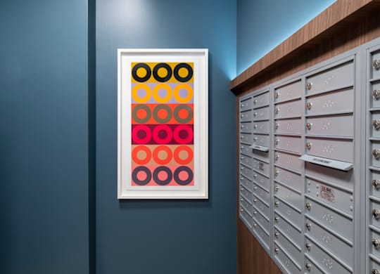A framed picture of circles in different colors is hanging on a wall next to a row of mailboxes.