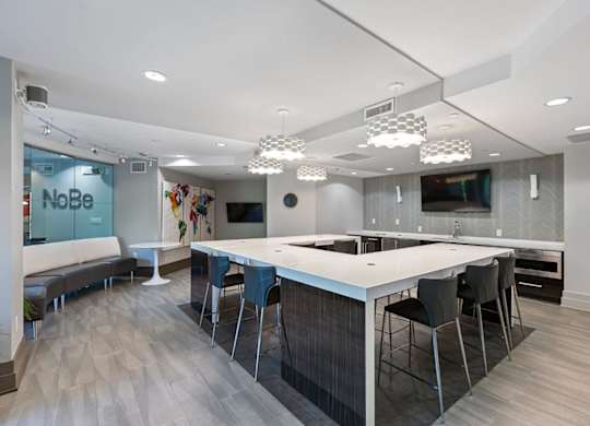 A modern kitchen with a long white island and black chairs.