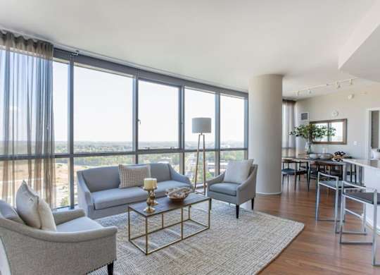 A living room with a grey couch, a grey armchair, a coffee table and a large window with a view of the beach.