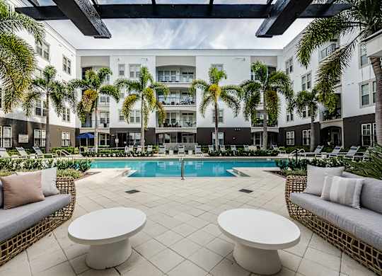 A pool surrounded by palm trees and white furniture.