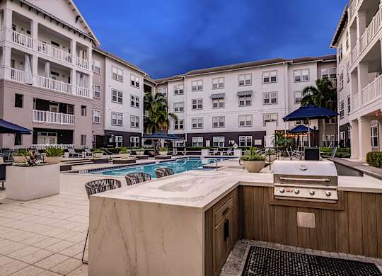 A poolside grill is in front of a pool and apartment buildings.