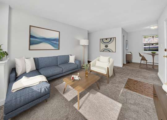 A living room with a blue couch, a white chair, and a painting on the wall.