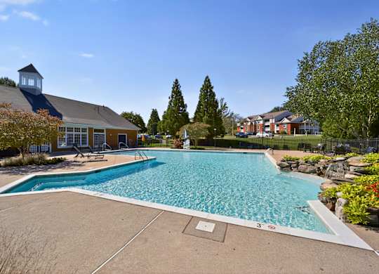 A large outdoor swimming pool surrounded by trees and a building.