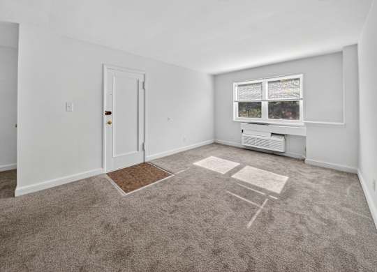 A room with a carpet, a door, a window with a view of trees and a small table.