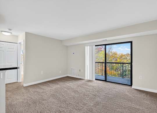 A spacious room with a carpeted floor and a sliding glass door leading to a balcony.