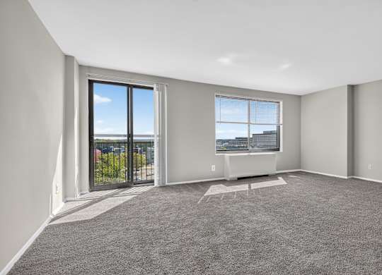 A spacious room with grey carpeting and large windows overlooking a parking lot.