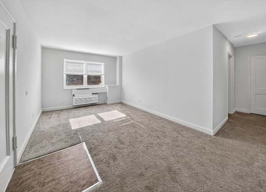 A room with a carpeted floor and a window with blinds.