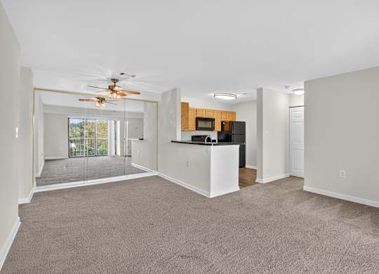 A spacious living room with a ceiling fan and a kitchen in the background.
