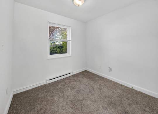 A room with a carpeted floor and a window showing a view of trees and a house.