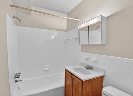 A white bathroom with a wooden vanity and a white toilet.