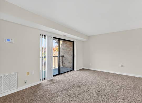 A room with a carpeted floor and a sliding glass door leading to a balcony.