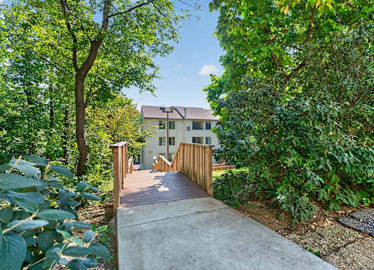 A wooden walkway leads to a white house surrounded by greenery.
