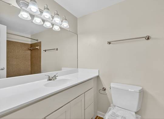 A white toilet sits in a bathroom with a white sink and mirror.