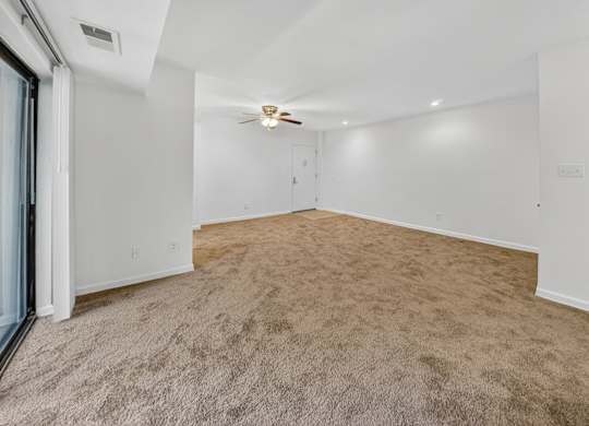 A room with a carpeted floor and a ceiling fan.