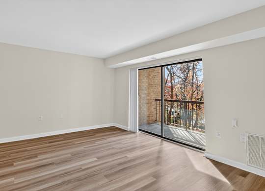 A room with wooden flooring and a sliding glass door leading to a balcony.