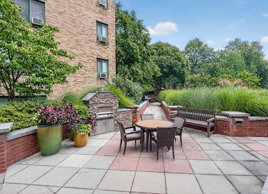 A patio with a table and chairs is surrounded by greenery.