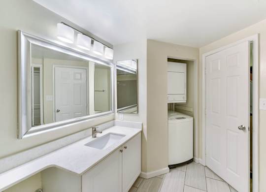 A white bathroom with a sink, mirror, and a white door.