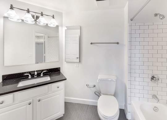 A white toilet sits in a bathroom next to a sink and a bathtub.