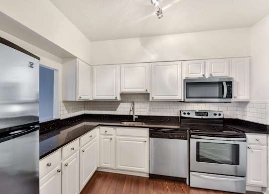 A kitchen with white cabinets and black countertops.