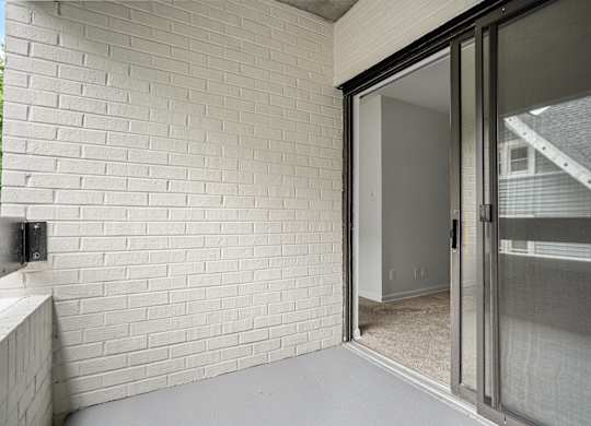 a sliding glass door opens to a patio in a home with a brick wall