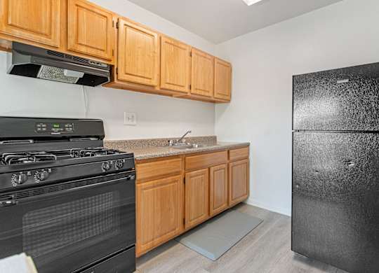 A black stove and refrigerator in a kitchen with wooden cabinets.