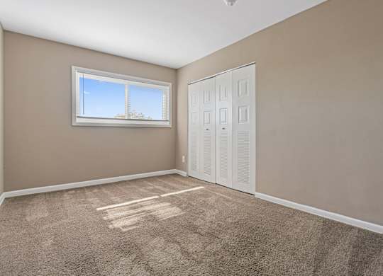 A room with a carpeted floor, a window, and a white door.