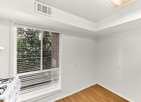 A room with a window covered by white blinds and a white gas stove.