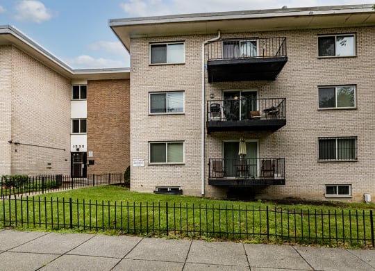 a brick apartment building with two balconies and a green lawn