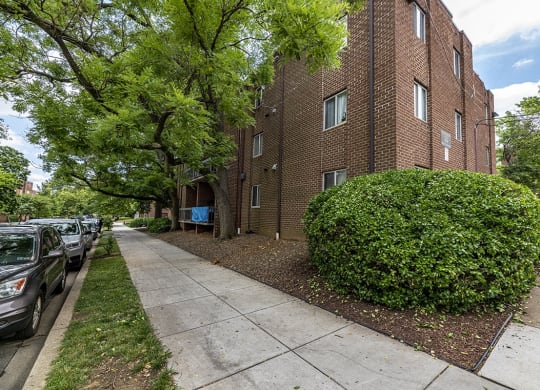 a brick apartment building with a sidewalk and trees