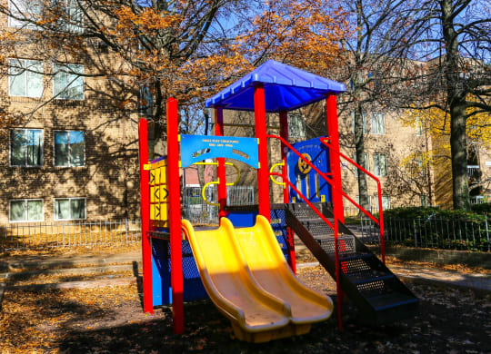 a playground with slides and a swing set in front of an apartment building