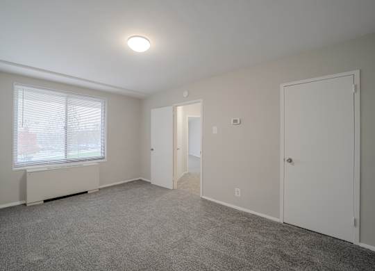 A room with a carpeted floor, a window with blinds, and a ceiling light.