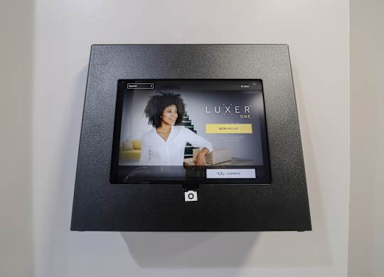 A black box with a screen displaying the word "LUXER" and a woman in the background.