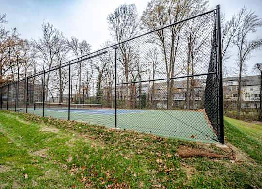 A tennis court is enclosed by a black fence.