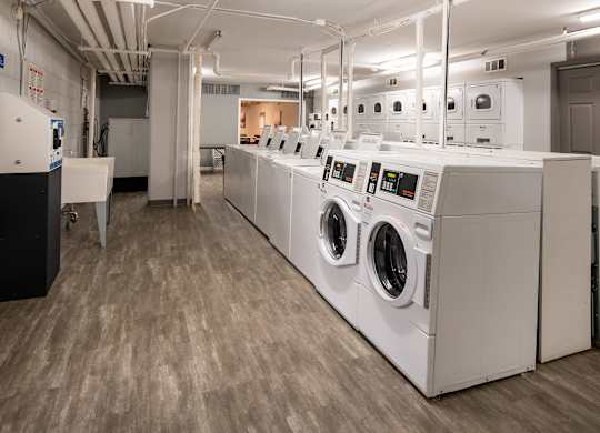 A row of industrial washing machines in a laundry room.