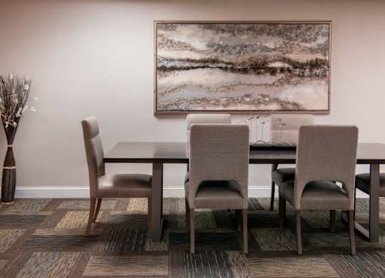 A brown dining table with four chairs and a vase with dried flowers.