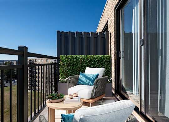 A balcony with a table, chairs, and a potted plant.