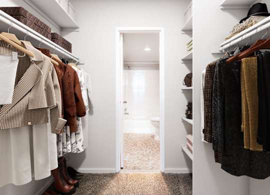 A hallway with a white door and clothes hanging on both sides.