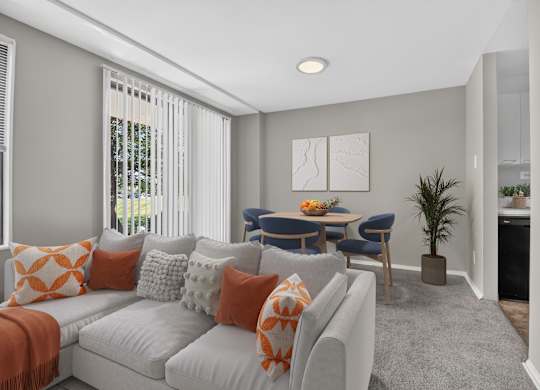 A living room with a grey couch, orange pillows, and a dining table with chairs.