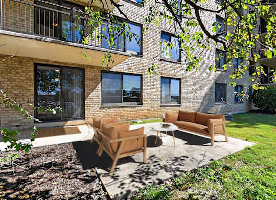 A patio with a couch and chairs is surrounded by a brick building.