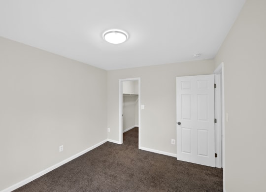 an empty bedroom with a white door and carpeted floor