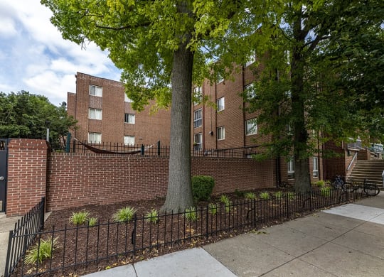 a brick building with a tree in front of a fence