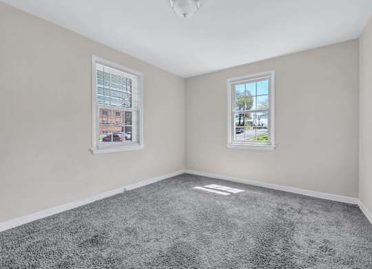 Empty bedroom with gray carpet and two windows at Highland Ridge Apartments, Capitol Heights