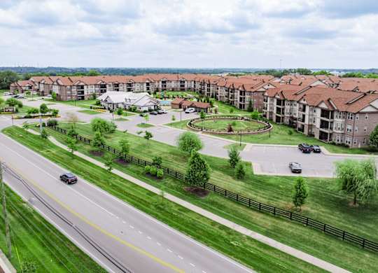 A road with cars and a grassy area with trees and apartment buildings in the background. at Century Belmont Station, Louisville, 40243